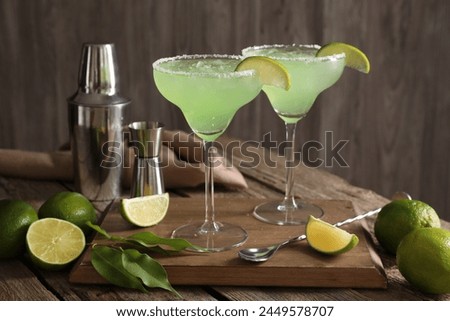 Delicious Margarita cocktail in glasses, limes and bartender equipment on wooden table