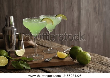 Delicious Margarita cocktail in glasses, limes and bartender equipment on wooden table