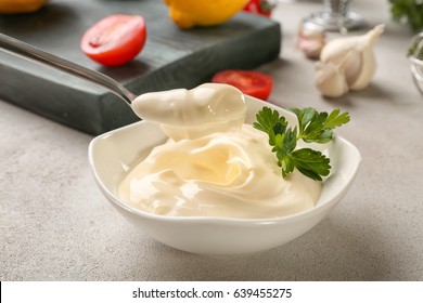 Delicious mayonnaise in bowl and spoon on kitchen table, closeup