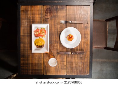 A Delicious Meat With Sauce And Tomato Salad Dish In Front Of A Steak Tartar Dish Next To A Cold Pint Of Beer On A Fancy And Rustic Wooden Table Ready For Lunch Or Dinnner