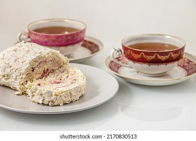 Delicious Meringue Roll With Strawberry Cream And Vintage Cups Of Tea On A White Glass Surface