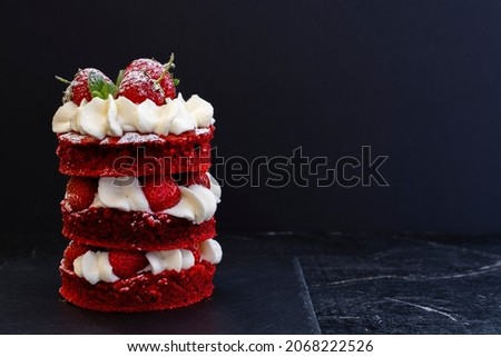 Delicious mini cake red velvet with white cream and strawberries on a saucer on a black wooden background. Food background. Gourmet dessert. Low key.