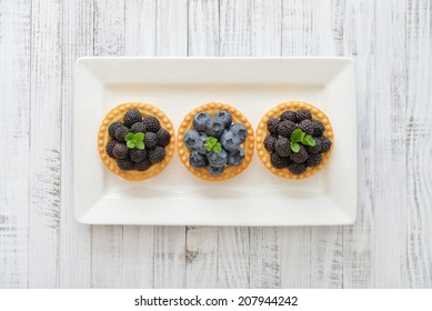 Delicious mini tart with fresh blackberries and blueberries on wooden background
