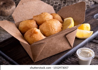 Delicious New England Style Clam Fritter Cakes In A Take Out Container On A Rustic Wood Table Top.