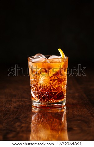 delicious old fashion cocktail in the etched glass with ice and orange slices, dark wooden background, vertical, side view