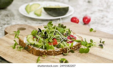 A delicious open-faced sandwich is displayed on a wooden board, featuring a generous layer of avocado, sliced tomatoes, and an abundance of vibrant microgreens - Powered by Shutterstock