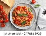 Delicious pasta with tomato sauce, basil and cheese on served gray textured table, flat lay