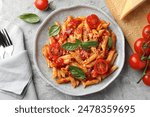 Delicious pasta with tomato sauce, basil and cheese on served gray textured table, flat lay