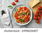 Delicious pasta with tomato sauce, basil and cheese on served gray textured table, flat lay