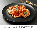 Delicious pasta with tomato sauce and basil served on black textured table, closeup