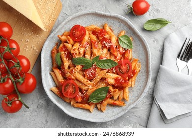 Delicious pasta with tomato sauce, basil and cheese on served gray textured table, flat lay