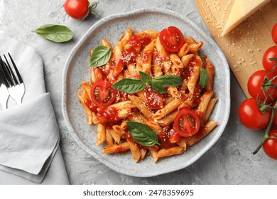 Delicious pasta with tomato sauce, basil and cheese on served gray textured table, flat lay