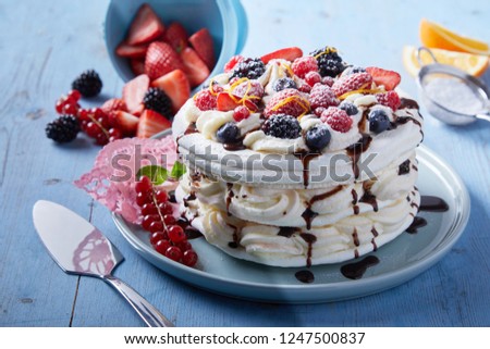 Delicious Pavlova cake with alternating layers of whipped cream and meringue topped with fresh berries and drizzled with chocolate syrup