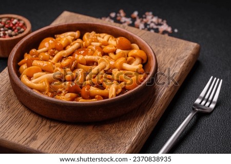Delicious pickled honey mushrooms with salt and spices in a ceramic plate on a dark textured background