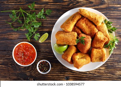 Delicious Pieces Of Crispy Fried Fish Coated In Batter And Coconut Bread Crumbs On White Plate On Old Charred Wooden Table, View From Above, Close-up