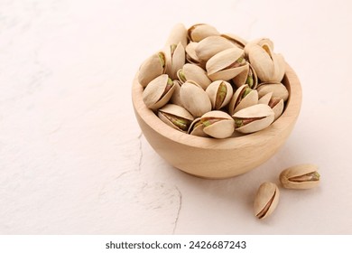 Delicious pistachios in bowl on white textured table. Space for text