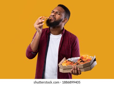 Delicious Pizza. African American Man Enjoying Eating Tasty Pizza Holding Pizzeria Box Standing Over Yellow Studio Background, With Eyes Closed. Cheat Meal, Nutrition And Fast Food Overeating.