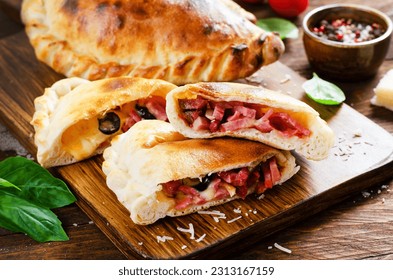 Delicious Pizza Calzone, Traditional Italian Pizza Stuffed with Ham and Cheese with Tomatoes and Fresh Basil on Wooden Background
