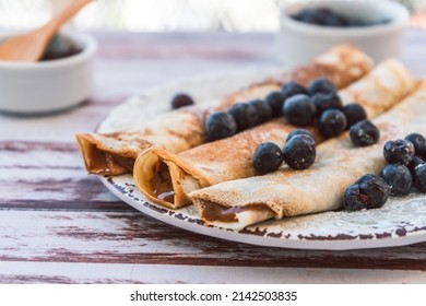 Delicious plate with homemade pancakes or crepes filled with dulce de leche and blueberries and icing sugar covering the plate.
