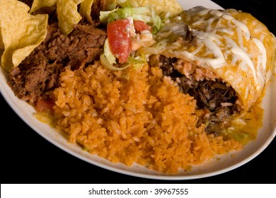 A delicious Plate of Mexican food. Close-up  of a smothered  burrito with Mexican rice, re-fried beans, chips and lettuce with tomatoes on a white plate.  Black background