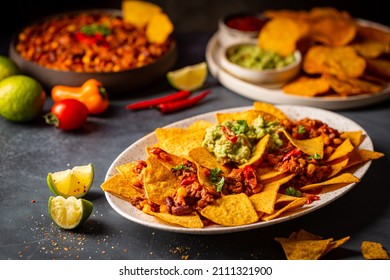 Delicious Plate Of Yellow Corn Nachos Chips With Cheese, Minced Meat And Red Hot Spicy Salsa Over Dark Background