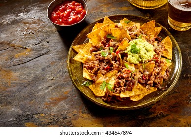 Delicious plate of yellow corn tortilla chips with cheese, meat, guacamole and red hot spicy salsa over table with copy space