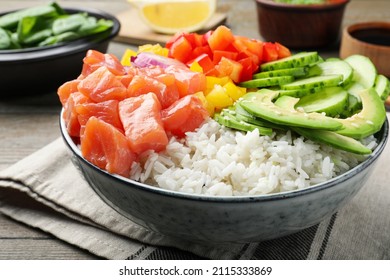 Delicious poke bowl with salmon and vegetables served on table, closeup