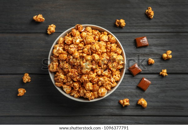Delicious popcorn with caramel in bowl and candies
on wooden background, top
view