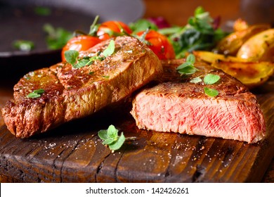 Köstliche Portion gesunden gegrillten, mageren, mittelseltenen Rindsteaks, das durchgeschnitten und auf einem mit frischen Kräuter gegarten Holzkochbrett serviert wird