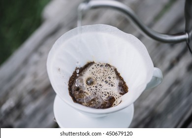 Delicious pourover coffee blossoming while man pours water into the dripper on the ground coffee beans. Summer picnic on the old wooden table background - Shutterstock ID 450679120