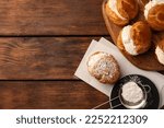 Delicious profiteroles with cream filling and powdered sugar on wooden table, flat lay. Space for text