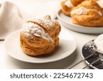 Delicious profiteroles with cream filling and powdered sugar on white table, closeup