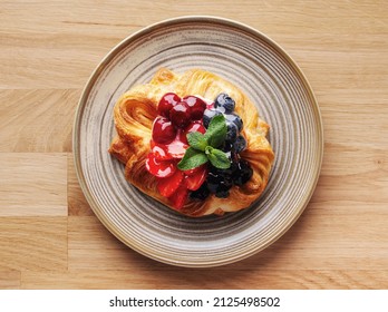 Delicious puff pastry with berries on plate on wood background. Puff pastry with strawberries, cherries, blueberries, blackberries, peaches, pineapple, cranberries and mint. Space for text. Close up. - Powered by Shutterstock