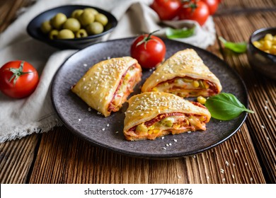 Delicious puff pastry pizza triangle rolls stuffed with tomato sauce, ham, cheese, corn, olives and sprinkled with sesame seeds