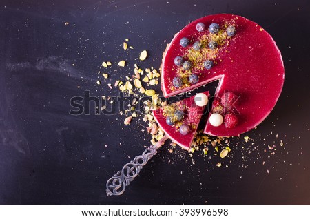 Delicious raspberry cake with fresh strawberries, raspberries, blueberry, currants and pistachios on wooden background. Free space for your text.