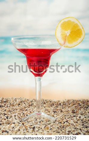 delicious red fruity cocktail on the sand with the sea beach ocean in the background