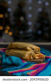 Delicious Red Meat Tamales, Wrapped In Tamale Leaves, To Celebrate Christmas In The Company Of The Family, In The Background A Beautiful Blur Of Christmas Lights, Vertical Photo.