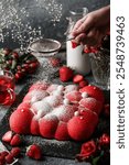 Delicious red milk mousse cake with sugar powder and strawberries on dark stone background with strawberries and flowers. Woman hand pouring powdered sugar. Sweets, dessert and pastry, close up