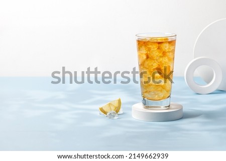 Delicious refreshing summer drink, iced tea in a glass on podium. Sunshine, blue background. Copy space. Ice tea, lemonade