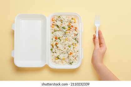 Delicious Rice With Vegetables In Container And Female Hand With Fork On Color Background