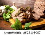 Delicious roasted cooked New Zealand spring lamb boneless. Wooden cutting board wood sliced slices carved juices. Mint sauce fresh leaves whole garlic. Side view rustic styling food photography. 