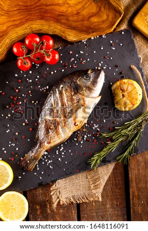 delicious roasted dorado or Gilt-head bream fish with lemon and orange slices, spices, and fresh rosemary on baking sheet, close-up