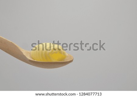Delicious roll of butter on a wooden spoon. Butter is used for cooking and baking and it adds a tasty flavor to the food. Picture is ideal for advertising dairy products,