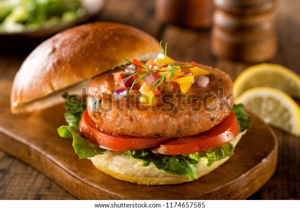 A delicious salmon burger with lettuce, tomato and\
pepper salsa with onion.