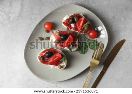 Delicious sandwiches with bresaola, cream cheese, olives and tomato served on light table, top view