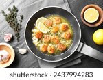 Delicious scallops with sauce in frying pan and ingredients on dark gray textured table, flat lay