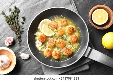 Delicious scallops with sauce in frying pan and ingredients on dark gray textured table, flat lay