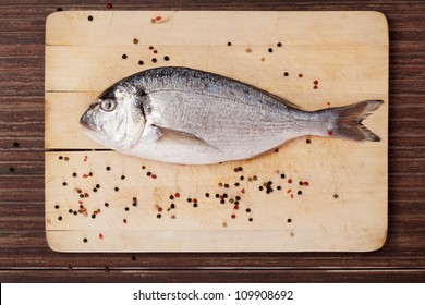 Delicious seafood concept in brown. Sea bream  on wooden chopping board with colorful peppercorns.