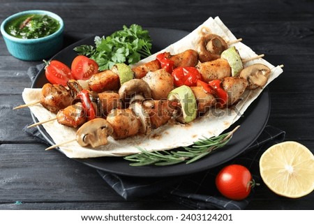 Delicious shish kebabs with vegetables served on black wooden table, closeup