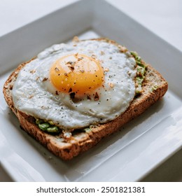 Delicious and simple breakfast dish: a perfectly cooked sunny-side-up egg placed on a slice of toasted whole-grain bread. The yolk is bright yellow and intact, surrounded by a slightly crispy white,  - Powered by Shutterstock